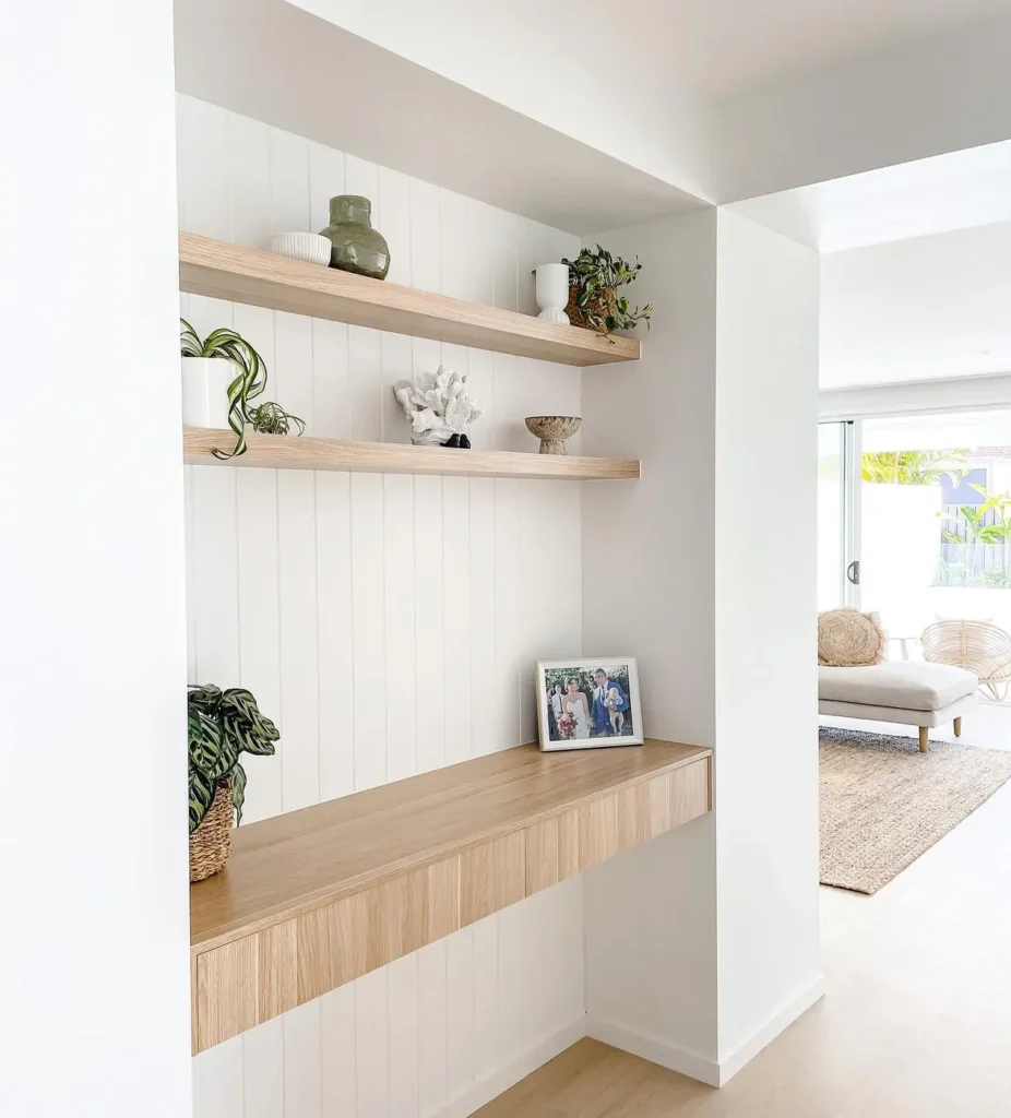 Bright entryway alcove with a floating wooden drawer, matching display shelves, and white wall panels.