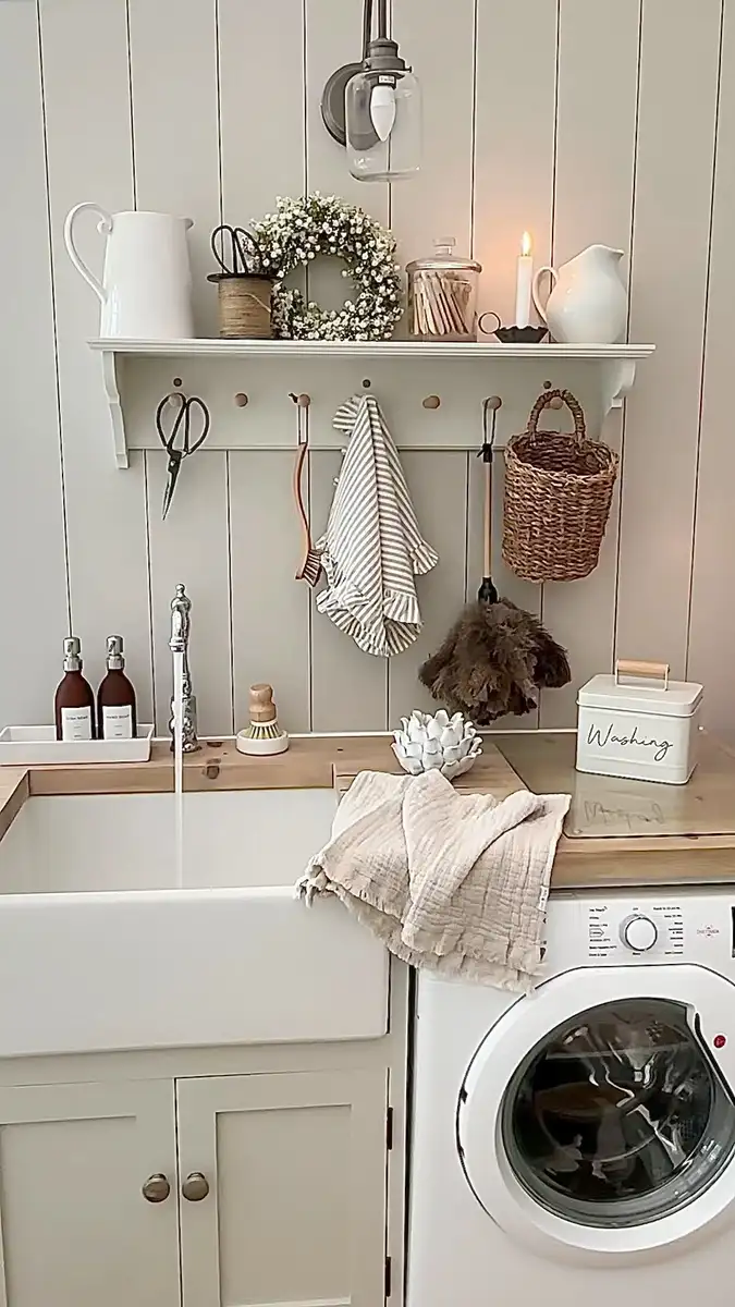 Cozy laundry sink wall with farmhouse sink, wood counter, peg shelf, hanging cleaning tools, small baskets, and front-loading washing machine.