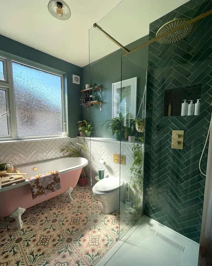 Colorful bathroom with a pink clawfoot tub, dark green herringbone shower, clear glass, and patterned flooring.