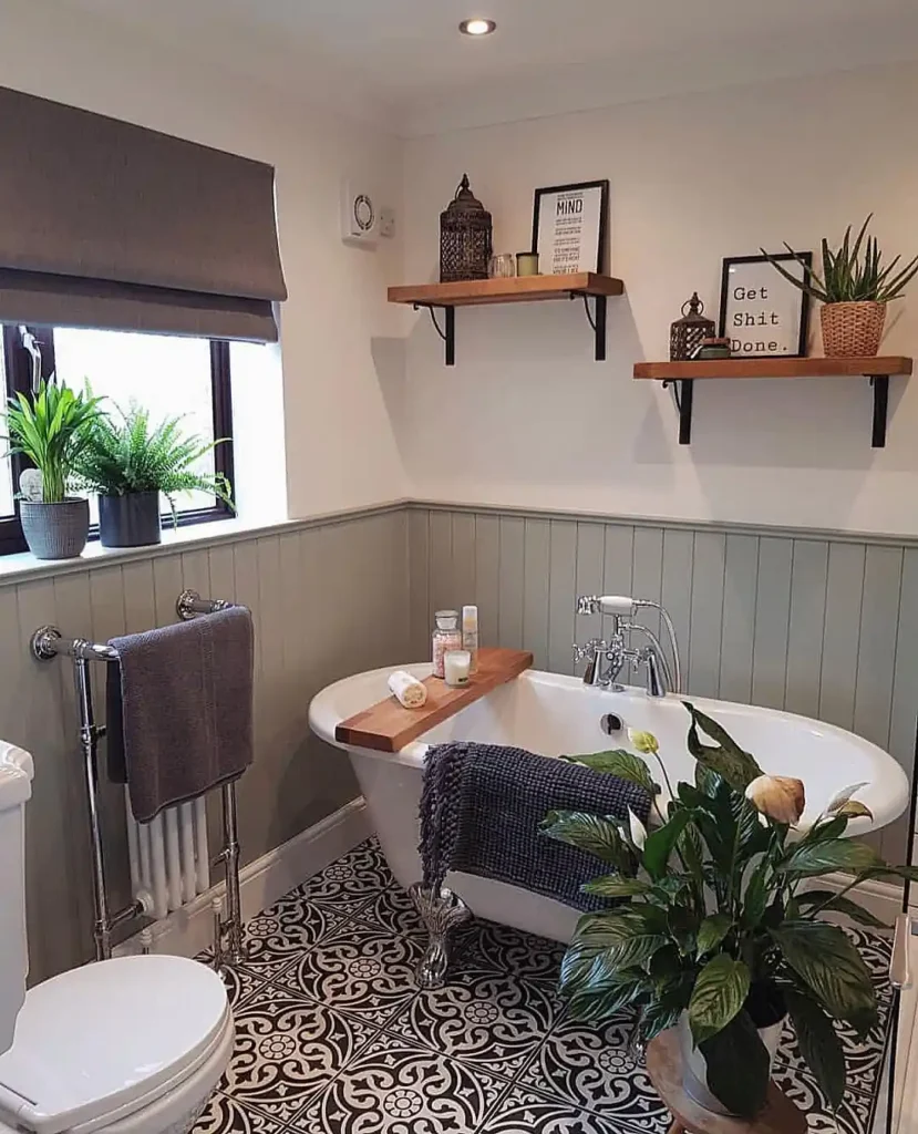 Warm wood bathroom wall shelves with black brackets, framed graphic prints, lanterns, candles, and potted greenery.