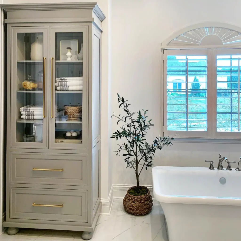 Tall bathroom cabinet with glass doors displaying neatly folded towels and lower drawers for hidden bathroom storage.