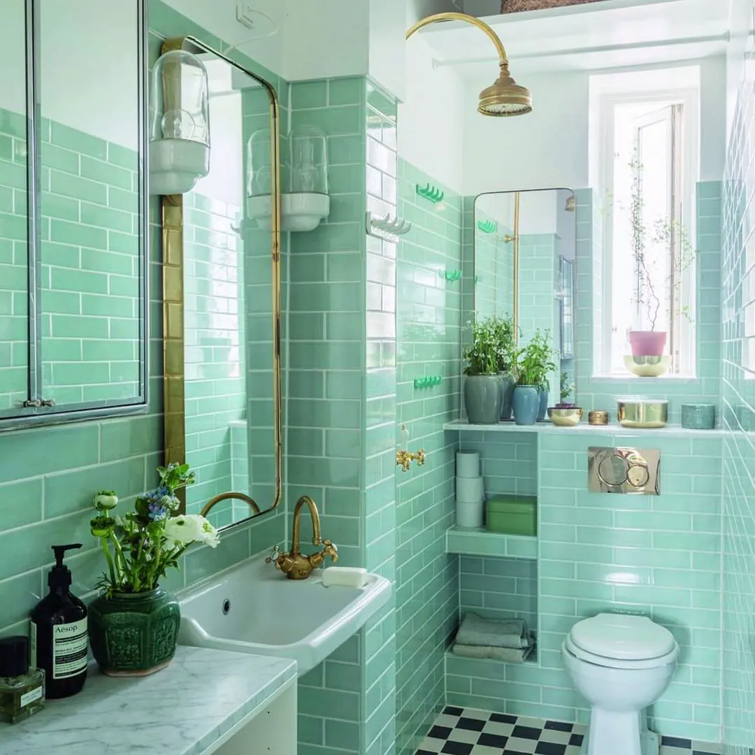 Olive green bathroom with floating wood shelves, round brass mirror, black vanity and lush houseplants