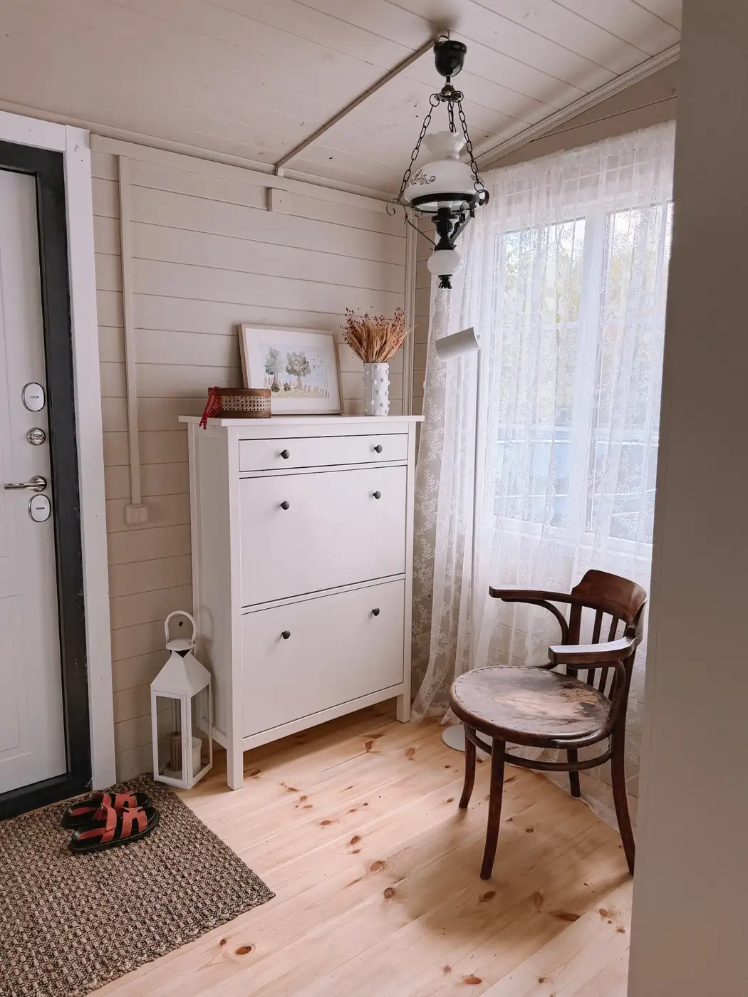 Tall narrow white entryway cabinet with closed shoe storage, top drawer, and nearby chair