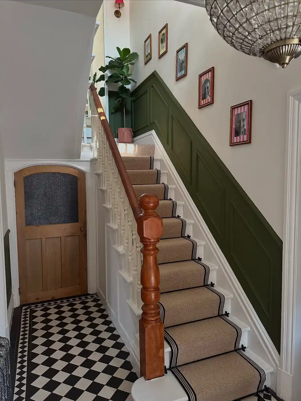 Stair hallway with deep green wall paneling, wood handrail, natural stair runner, white trim, and framed photos