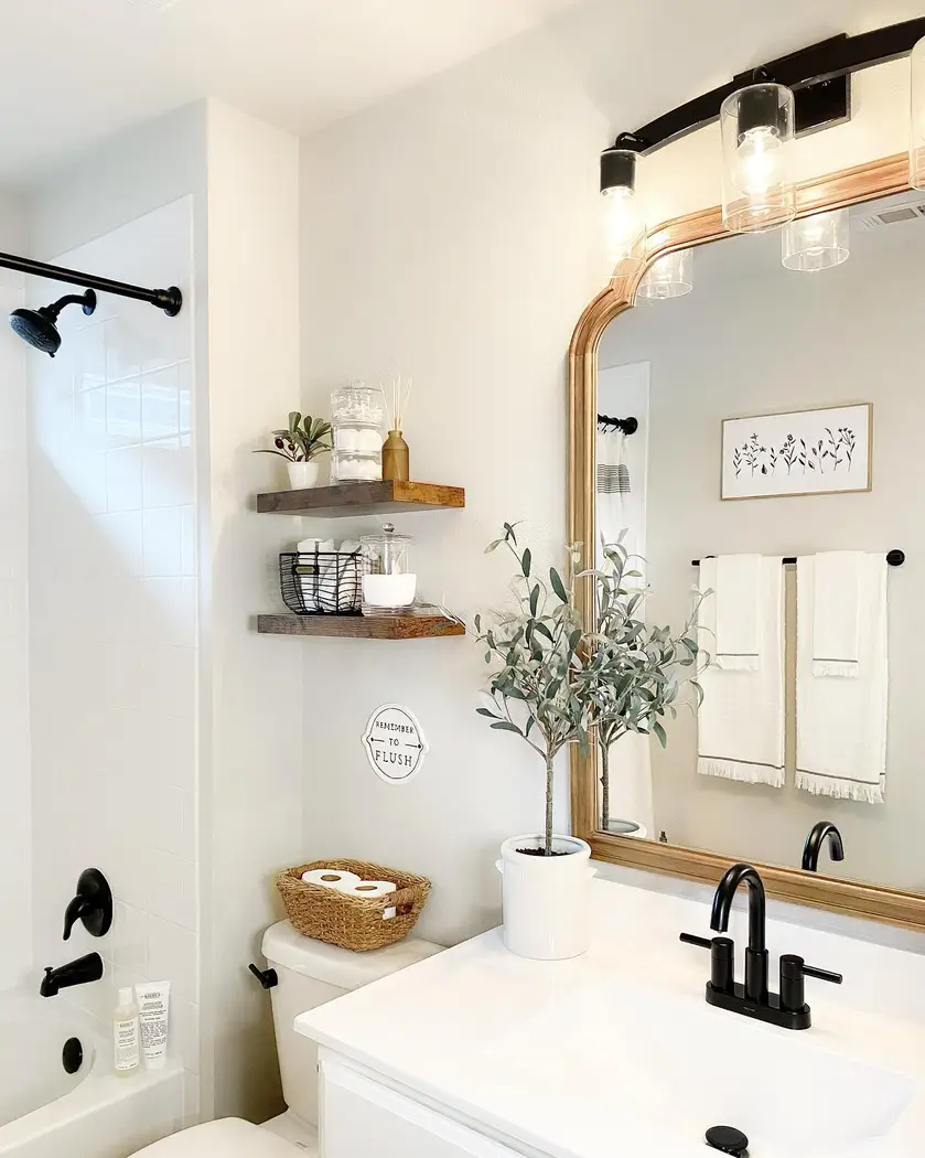 Bright modern farmhouse bathroom with white vanity, warm wood mirror and shelves, black fixtures, woven storage, and greenery