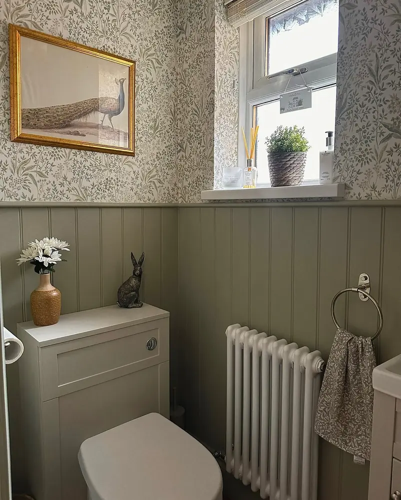 Small sage powder room with a concealed toilet tank, vertical paneling, botanical wallpaper, and a white radiator.