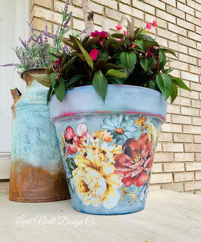 Dusty blue flower pot decorated with layered vintage style flowers in cream, coral, red, and yellow
