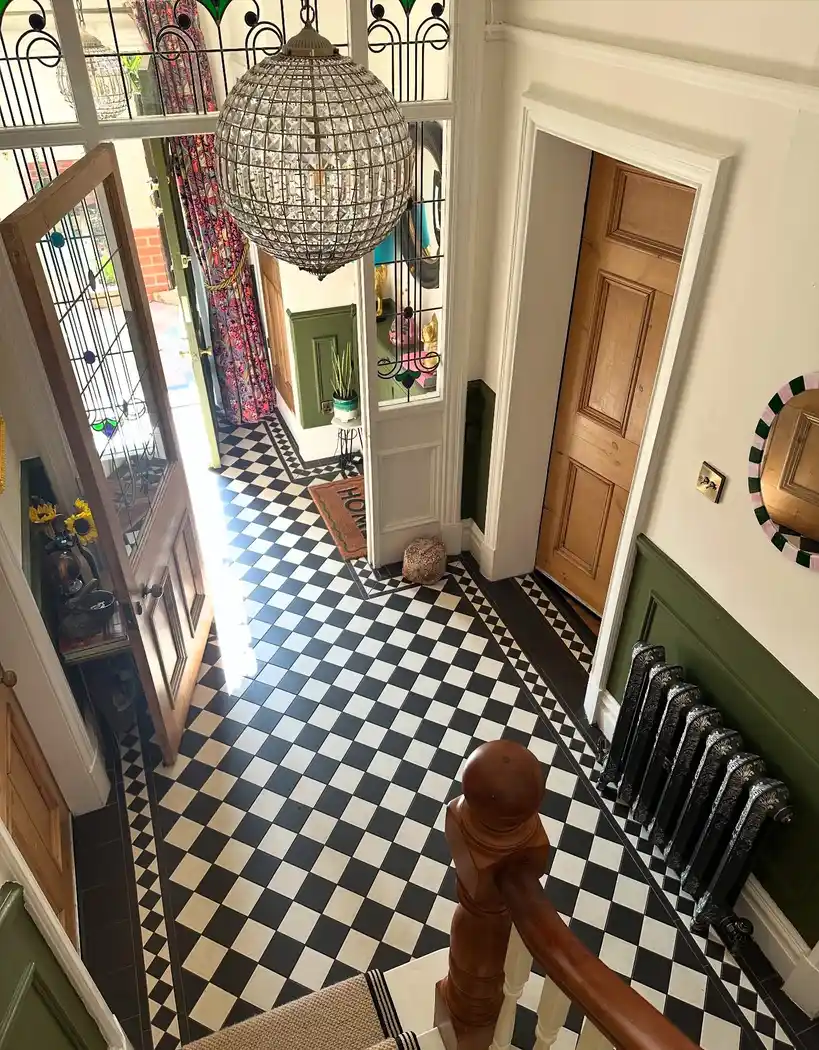 Hallway with bold black and white checkerboard floor, warm wood doors, deep green walls, and statement pendant