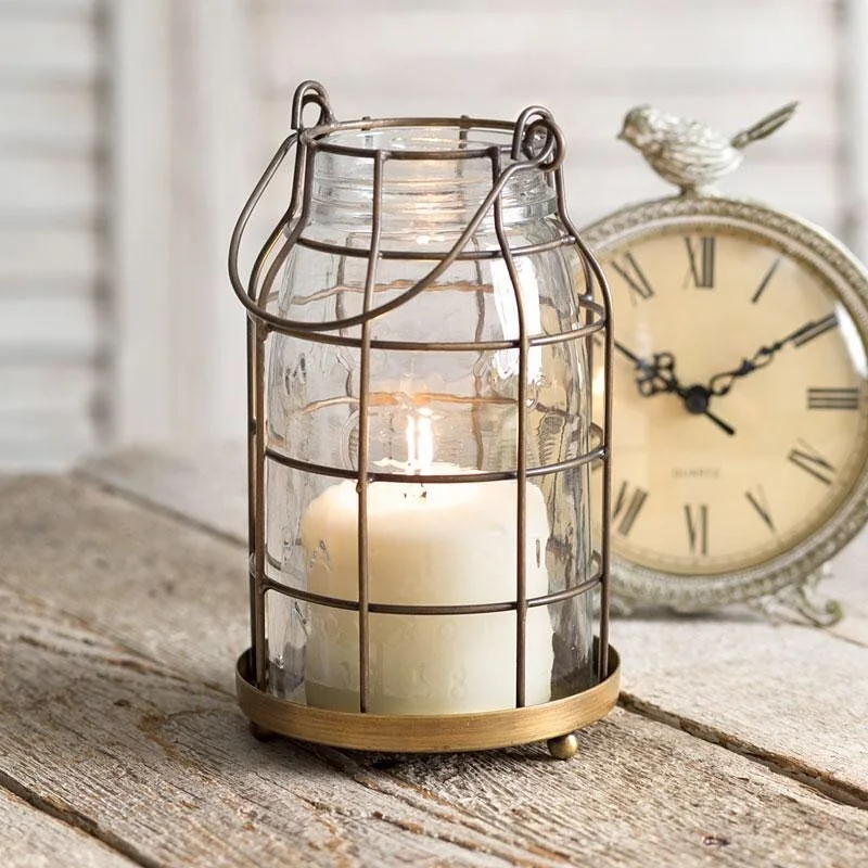 Clear mason jar candle lantern displayed inside a rustic aged metal cage on a wooden surface