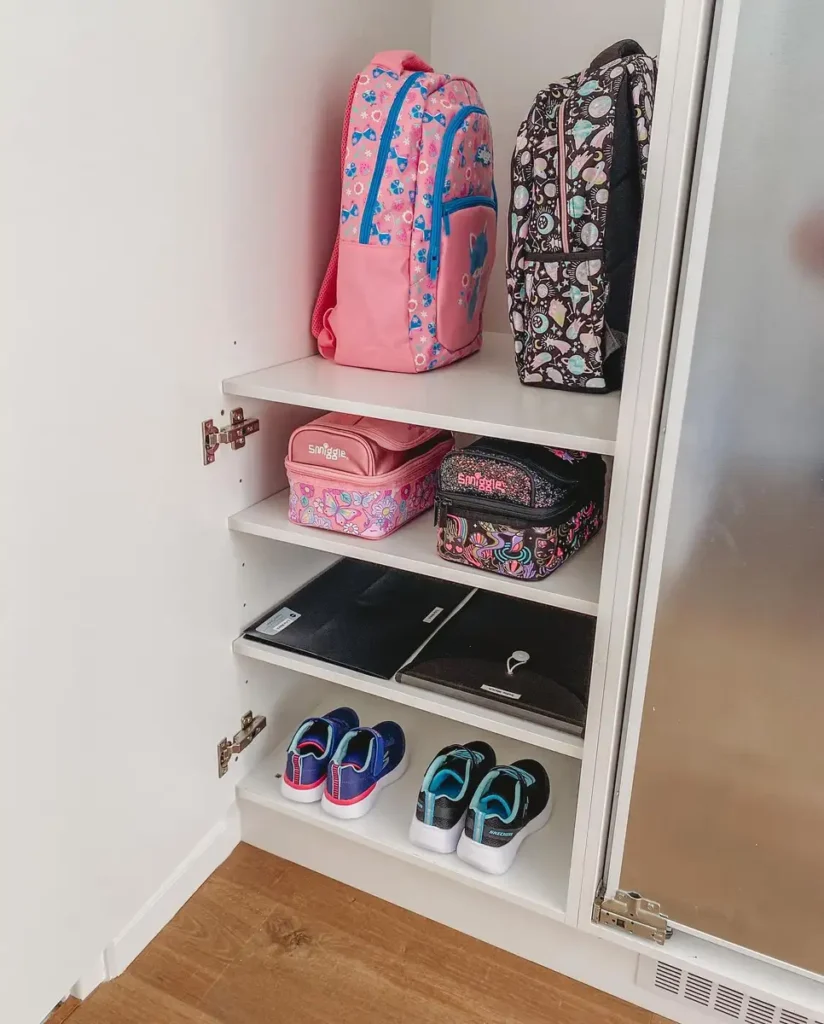 Closed entryway cabinet organized with backpacks, lunch bags, school folders, and children’s shoes on separate shelves.