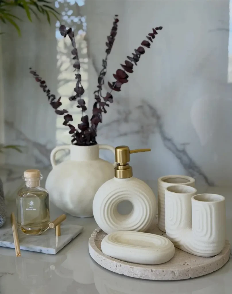 Round stone-look tray with a cream soap dispenser, matching cups and oval soap dish against a marble wall.