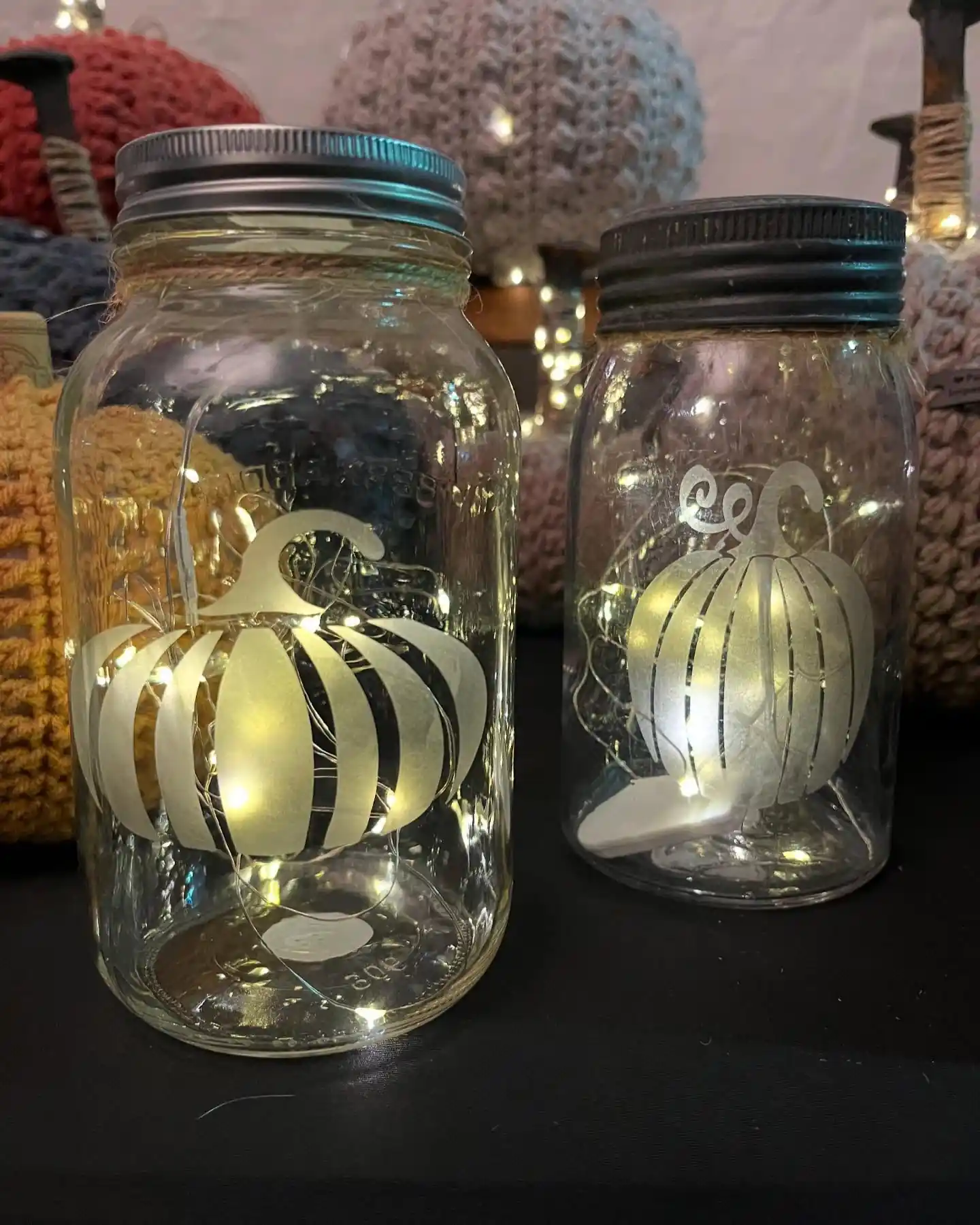 Two mason jars with white pumpkin cutouts glowing from warm fairy lights inside