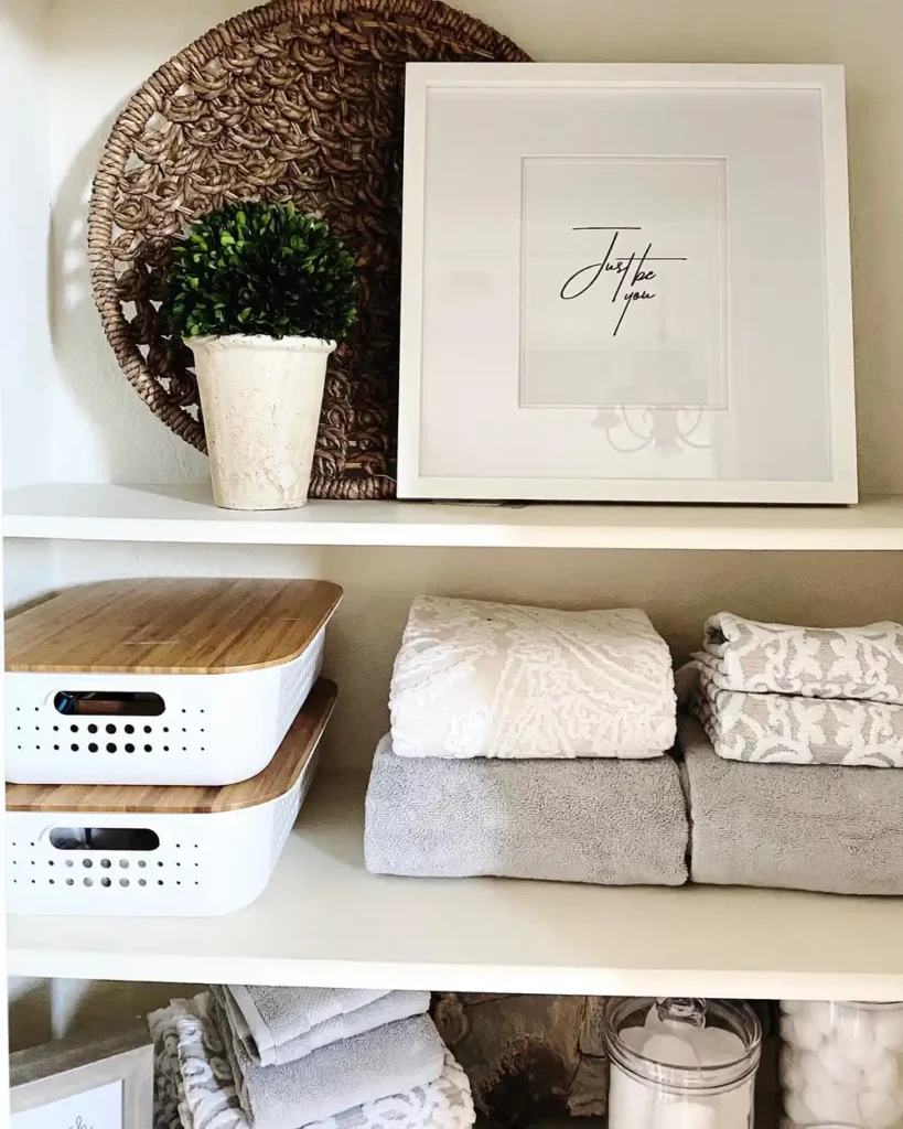 Bathroom linen closet with folded white towels and shallow white storage bins topped with natural wood lids.