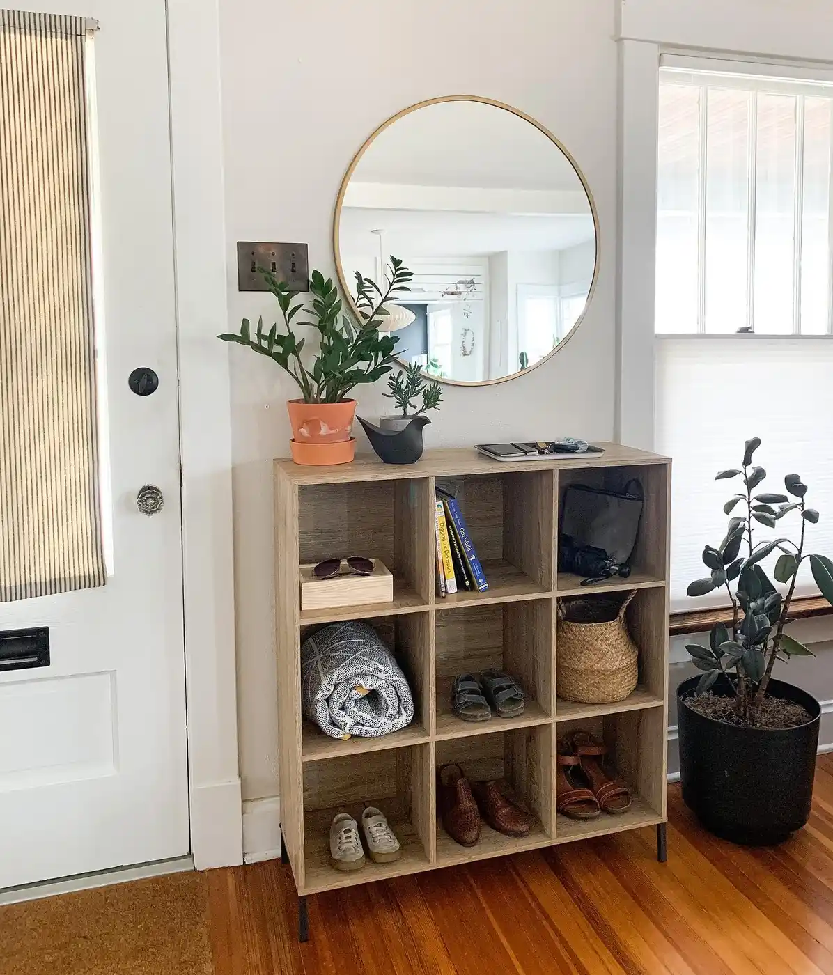Cube shelf entryway organizer with shoes, baskets, bags, books, tray, and round wall mirror