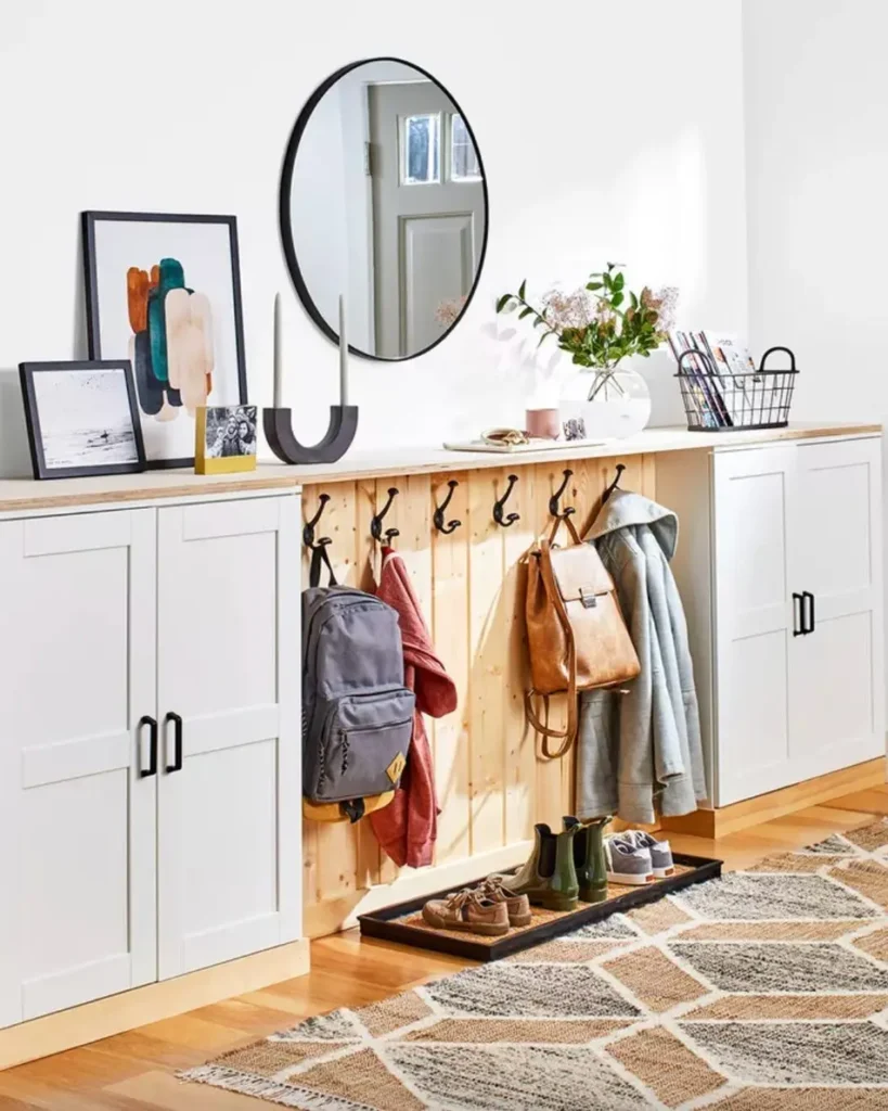 Entryway drop zone with white storage cabinets, an open wooden hook rail, and a round mirror.