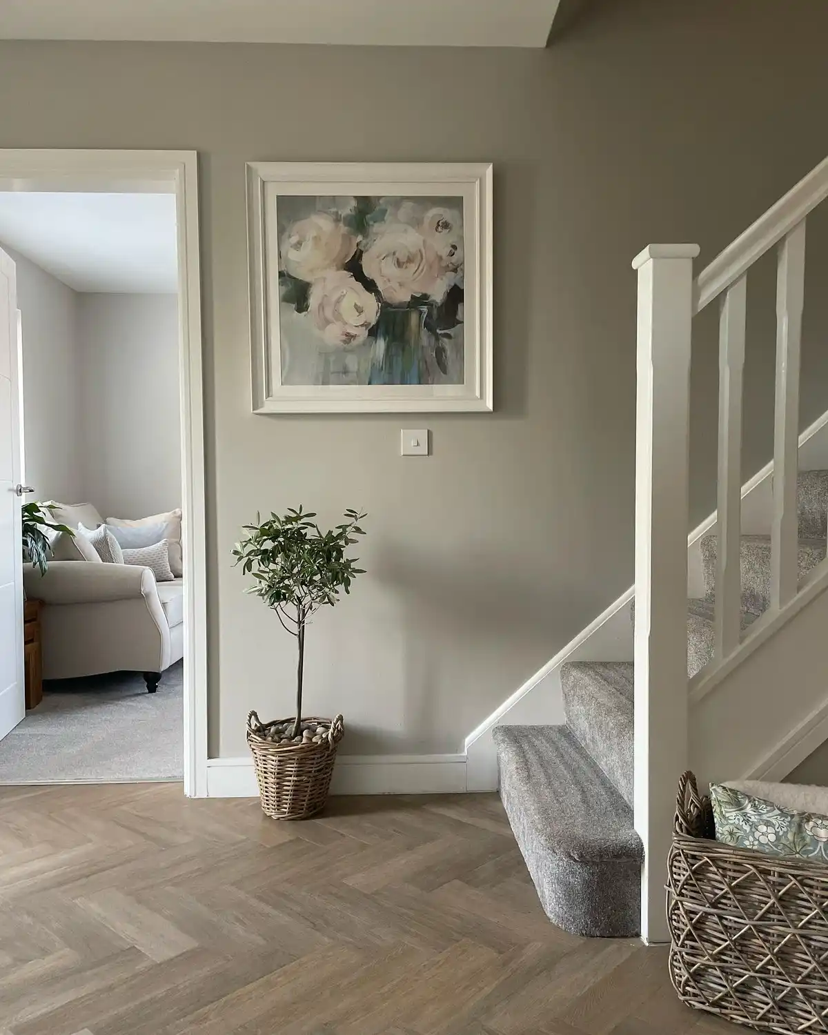 Simple stair landing with framed floral artwork, small potted tree, woven basket, gray walls, and patterned floor