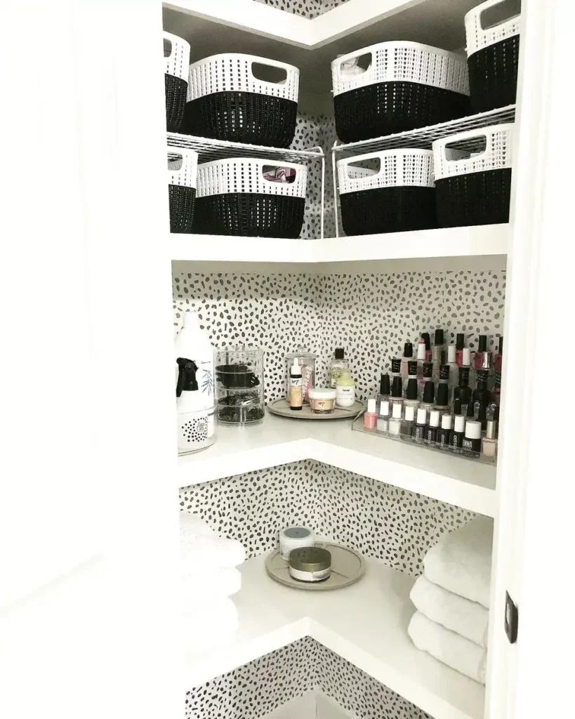 Corner bathroom closet with woven baskets, tiered clear organizers for beauty products, and neatly folded white towels.