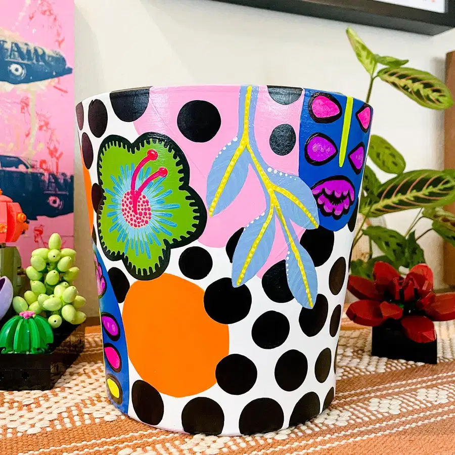 White flower pot covered with bold black polka dots, colorful abstract shapes, leaves, and floral motifs