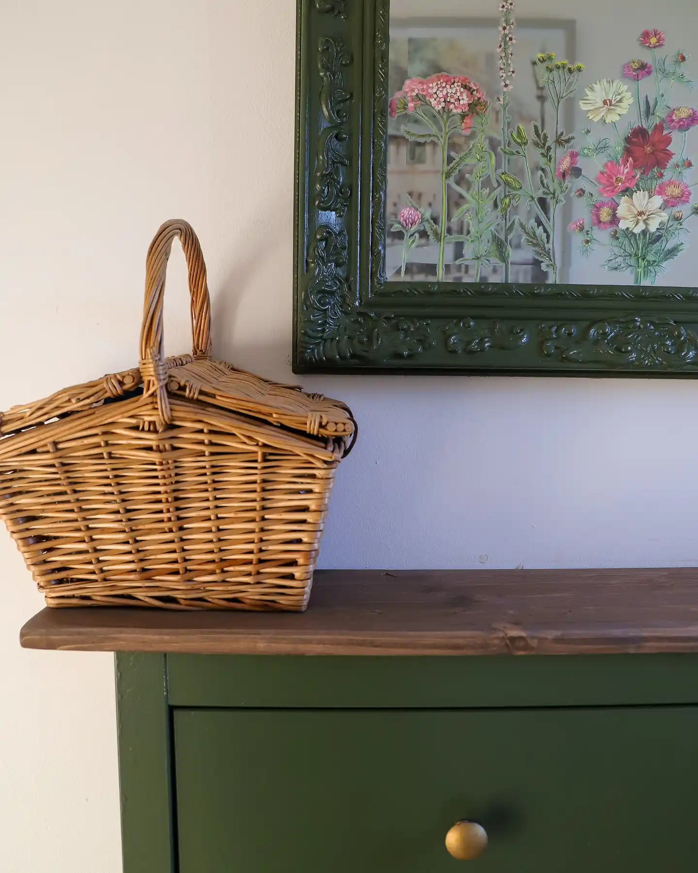 Hallway with deep green cabinet, ornate green mirror, dark wood top, wicker basket, and reflected floral arrangement