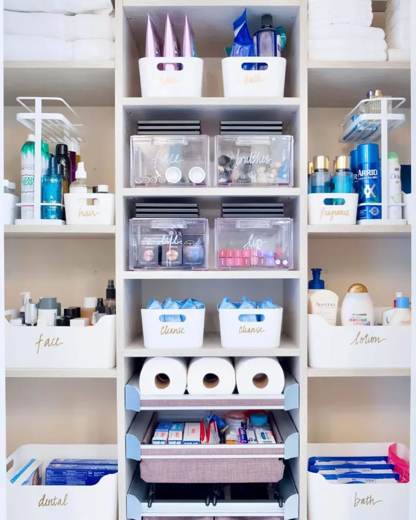 Highly organized bathroom closet with labeled clear bins, drawers, beauty products, toiletries, first aid supplies, and backstock.