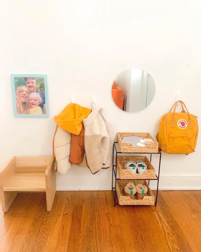 Kid-height entryway station with backpack hook, coat hooks, small chair, mirror, and basket shoe storage.