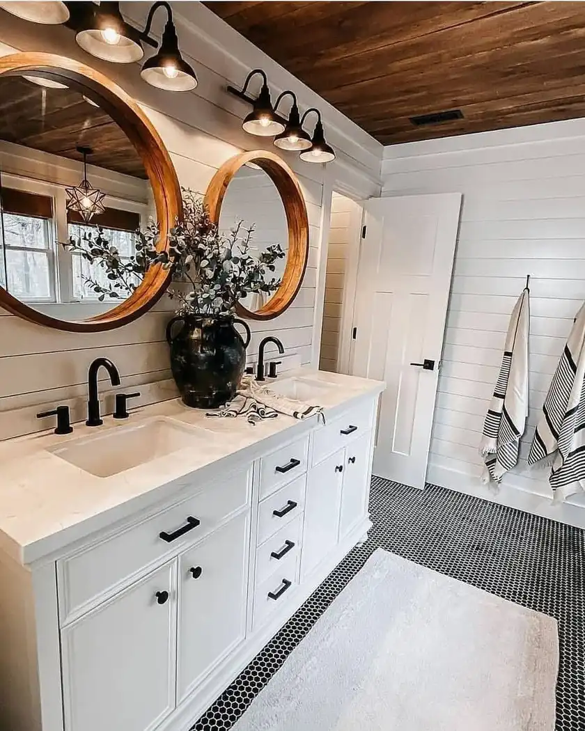Modern farmhouse bathroom with rich wood plank ceiling, white shiplap walls, double vanity, round wood mirrors, black fixtures, and penny tile floor