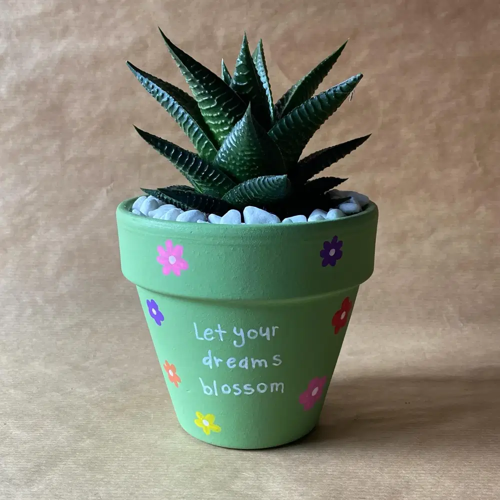 Soft green flower pot painted with a short inspirational message and small colorful flowers