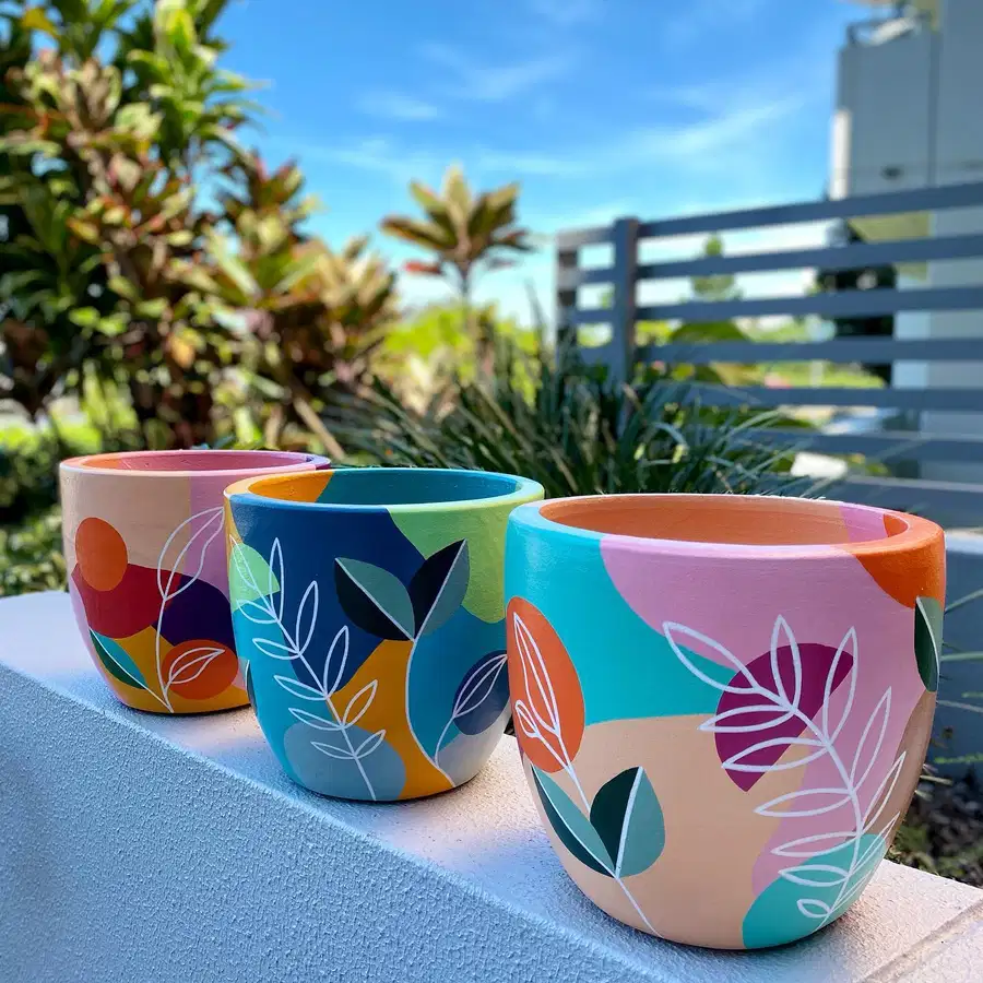 Colorful flower pots painted with abstract blocks of pink, teal, orange, and navy with white leafy branches
