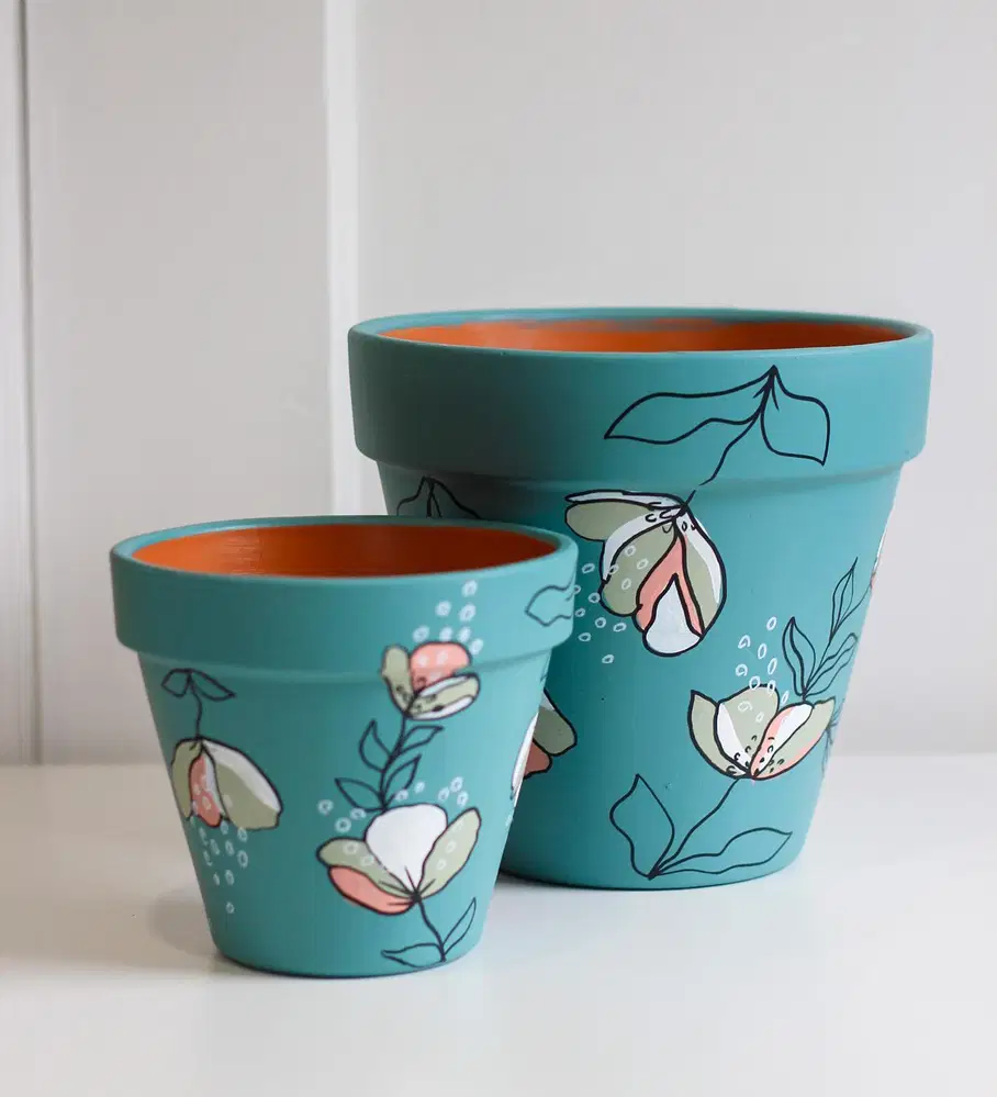 Teal flower pots decorated with soft peach, sage, and white flowers mixed with fine black botanical outlines