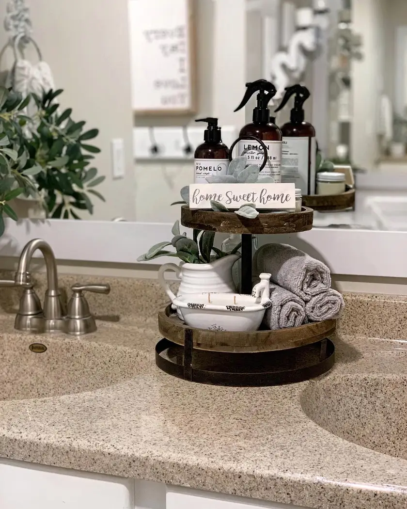 Modern farmhouse bathroom vanity with two-tier rustic wood tray, rolled gray towels, amber bottles, and greenery