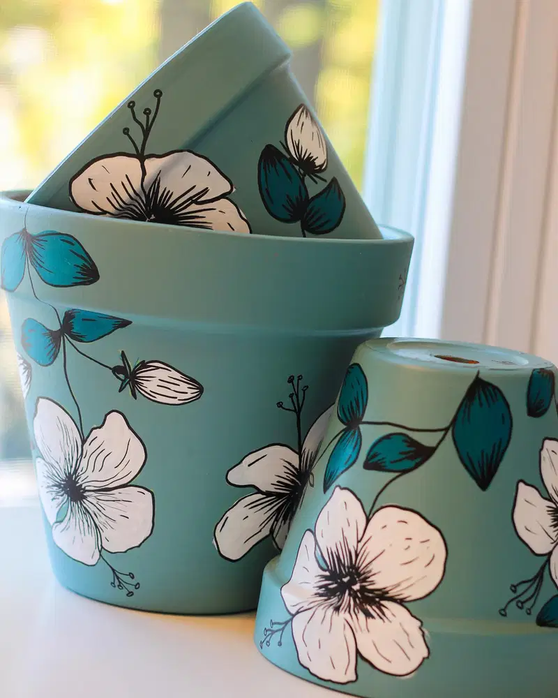 Teal flower pots decorated with white floral illustrations, blue leaves, and black outlines