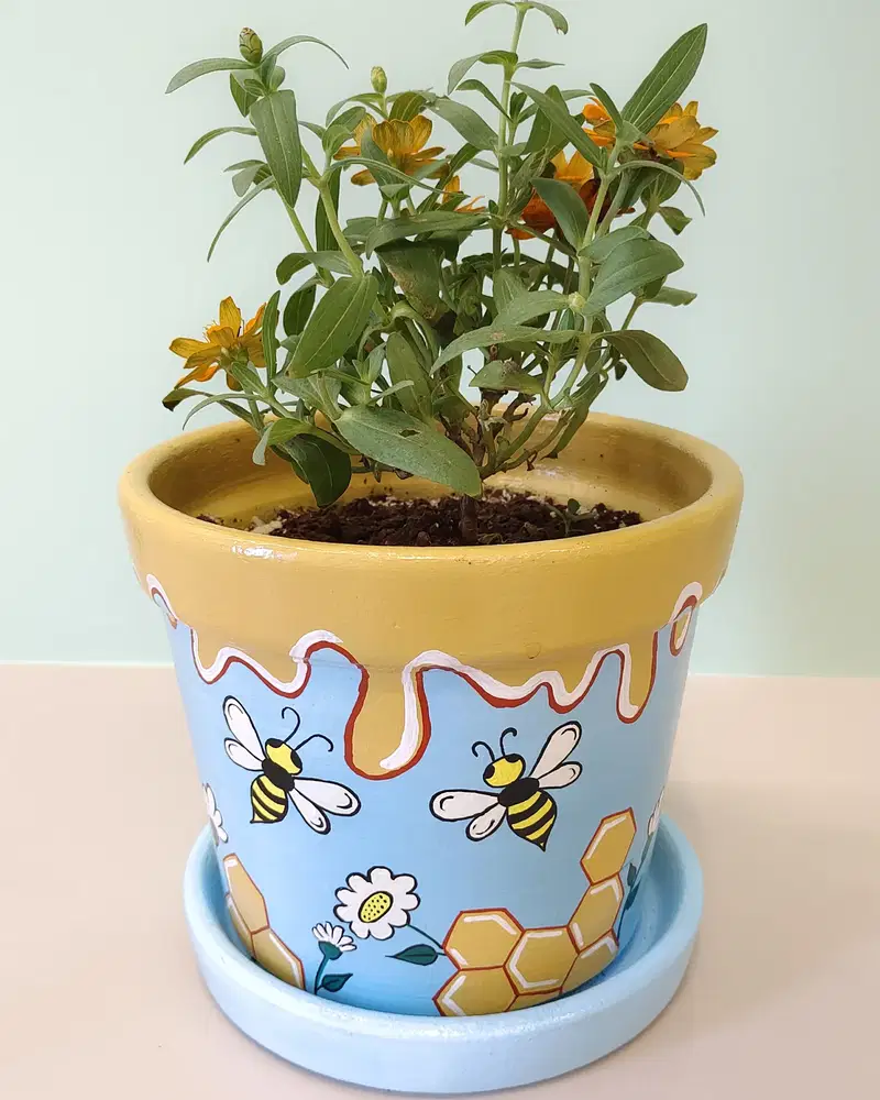 Blue flower pot painted with bees, daisies, honey drips, and yellow honeycomb shapes