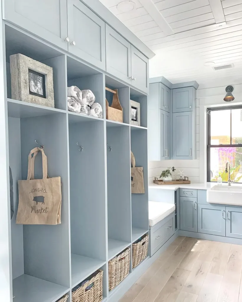 Soft blue drop zone with tall personal cubbies, wall hooks, upper cabinets, and lower storage baskets.