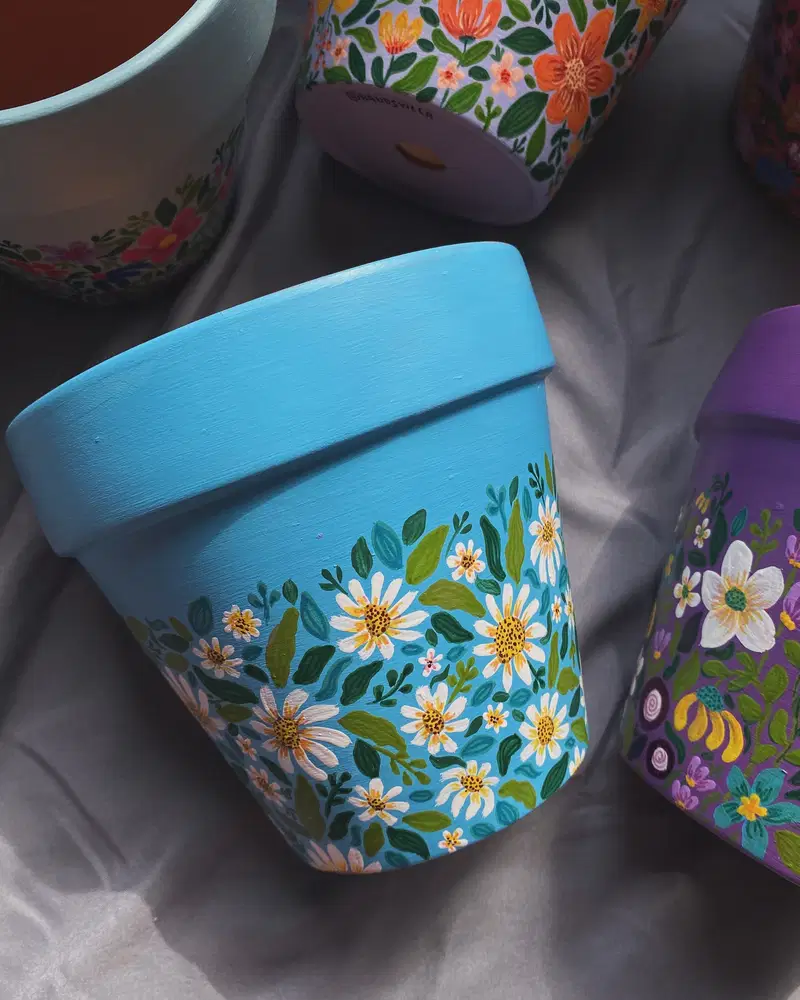 Bright turquoise flower pot covered with white daisies, tiny flowers, and layered green leaves