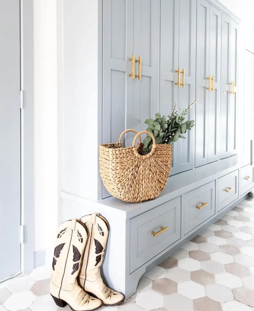 Pale blue entryway cabinets with brass handles, a long bench, and wide shoe drawers underneath.