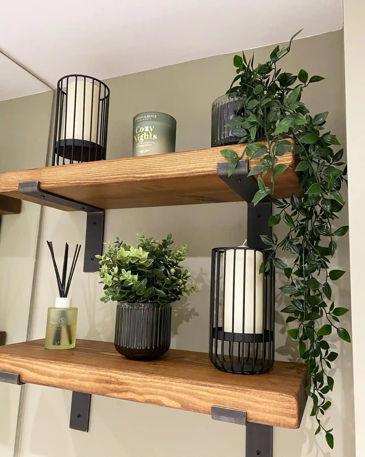 Guest bathroom wall with thick wood floating shelves, black brackets, trailing greenery, candle, diffuser and lantern decor