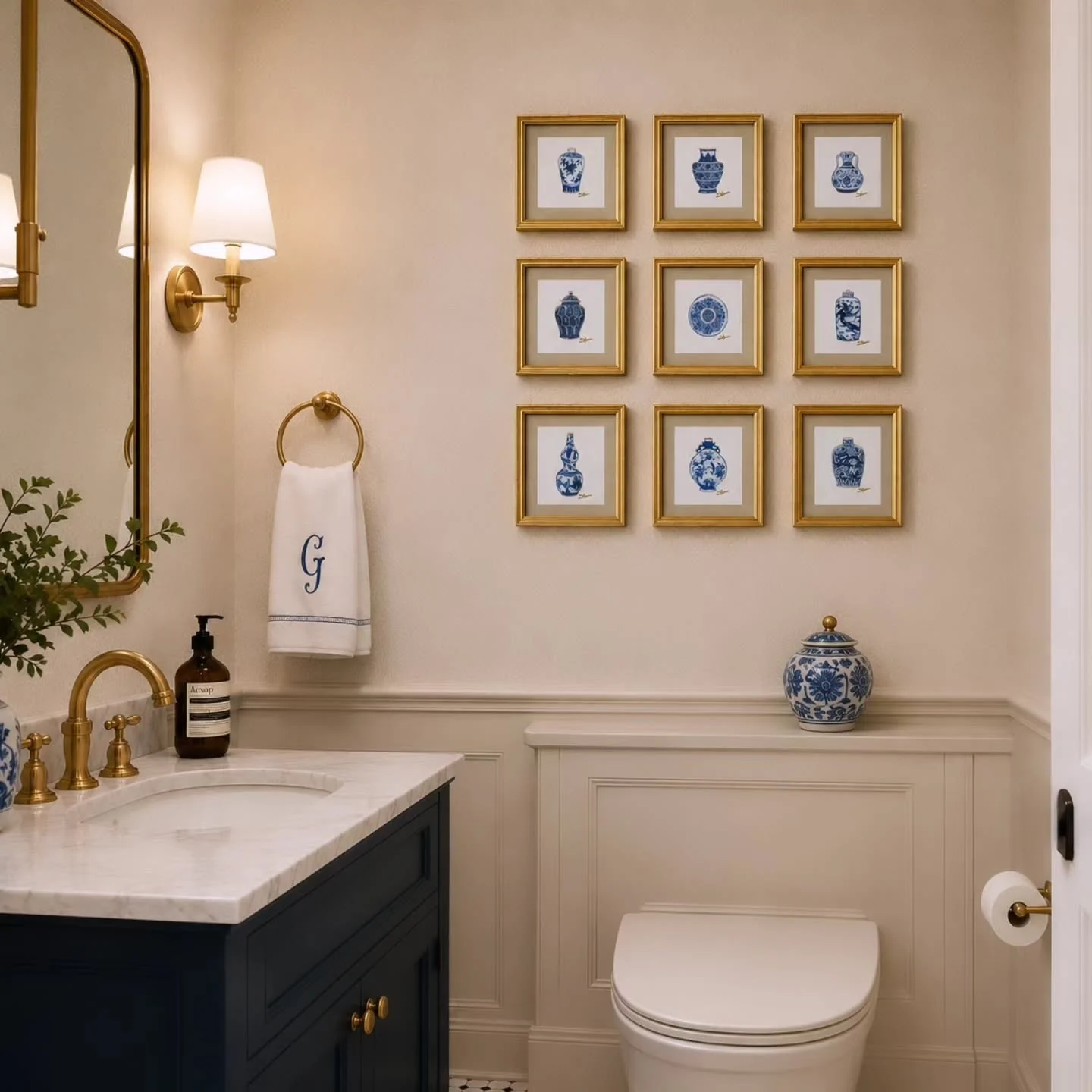 Classic guest bathroom with navy vanity, blue and white gallery wall, gold frames, brass fixtures and monogrammed hand towel