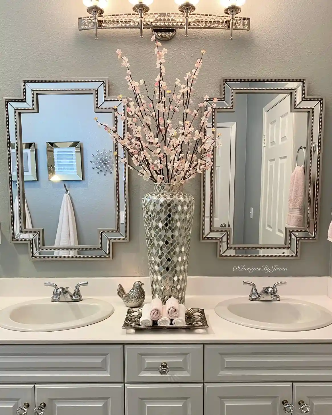 Double sink guest bathroom with matching silver mirrors, tall pink blossom arrangement, rolled hand towels and gray vanity
