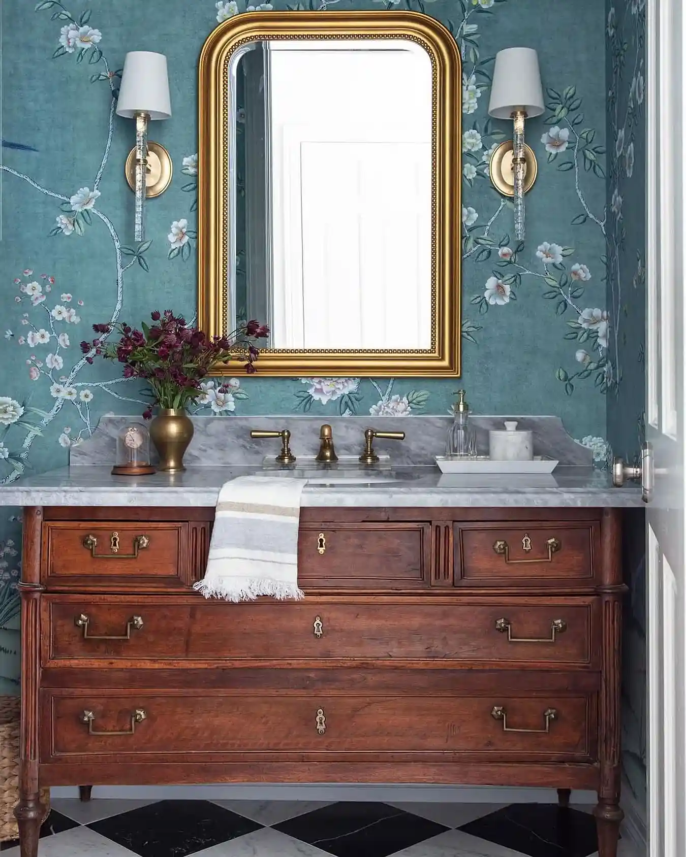 Elegant guest bathroom with teal floral wallpaper, antique wood vanity, marble countertop, gold mirror and brass fixtures