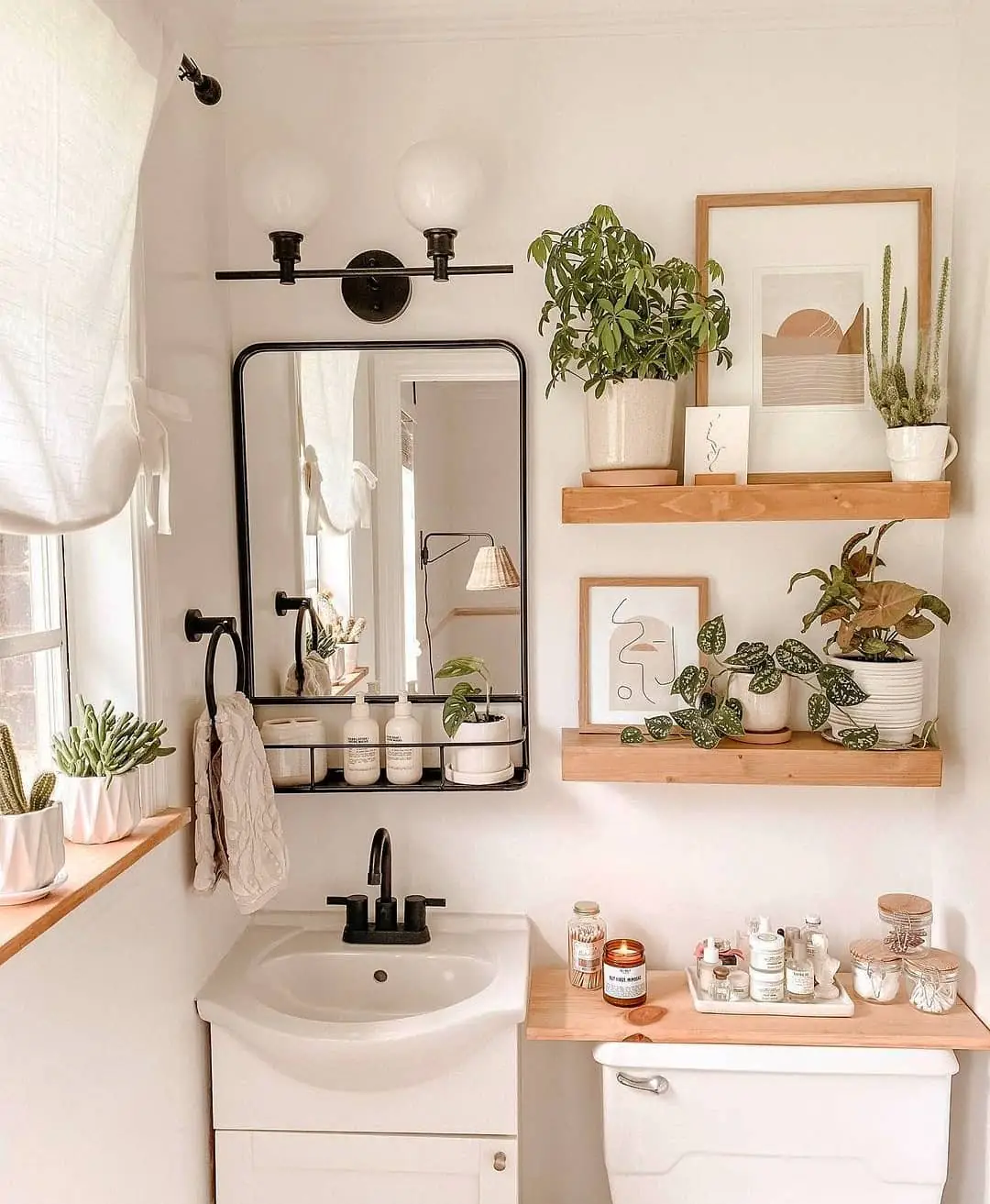 Small guest bathroom with wood floating shelves, framed art, green plants, black mirror, toiletries and guest essentials