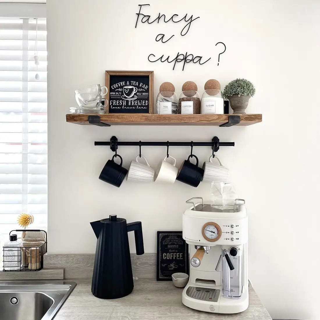 Wall-mounted coffee station with floating wood shelf, hanging mugs, espresso machine, kettle, and labeled coffee jars