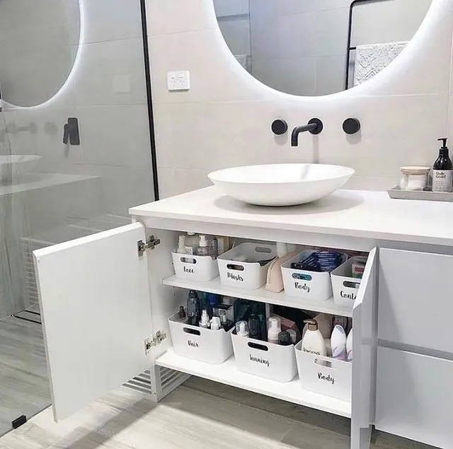 Under bathroom sink organized with labeled open bins for hair products, body care, toiletries, and everyday bathroom essentials