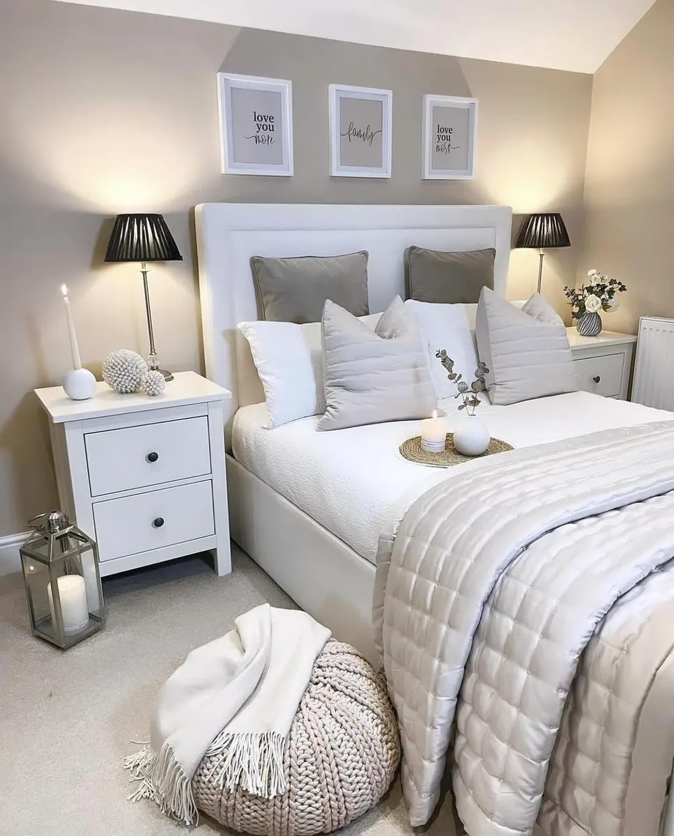 Neutral bedroom with white bedding, taupe pillows, black bedside lamps, and framed wall art above the bed.