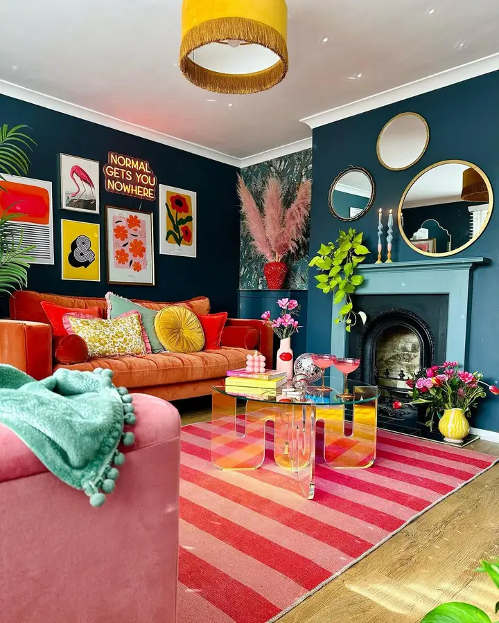 Colorful living room with deep teal walls, orange velvet sofa, pink striped rug, bright artwork, and yellow lighting