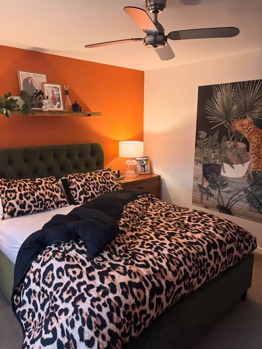 Leopard print bedding on a dark green upholstered bed against a burnt orange bedroom wall