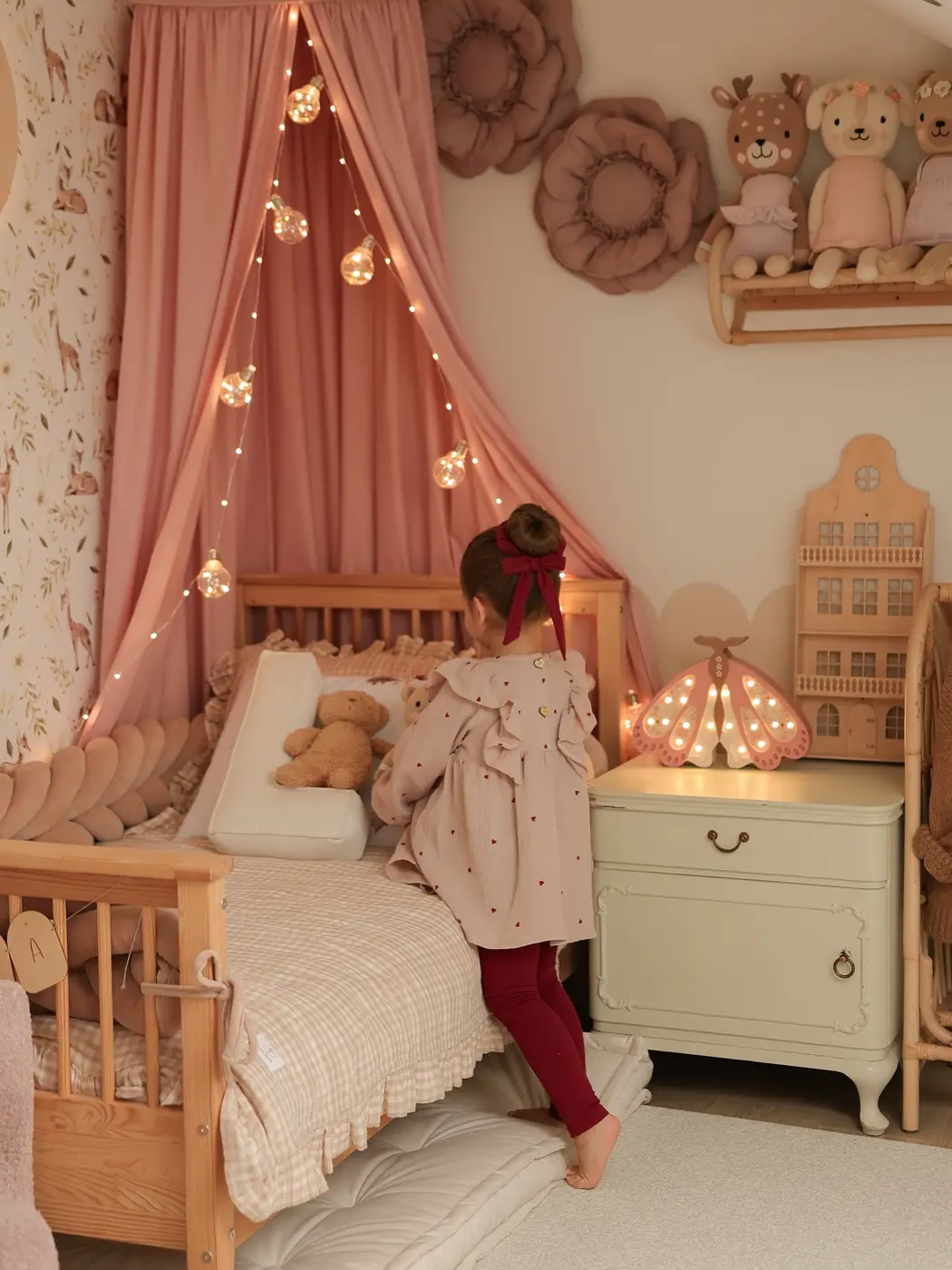 Wooden girls bed framed with dusty pink draped fabric and warm string lights