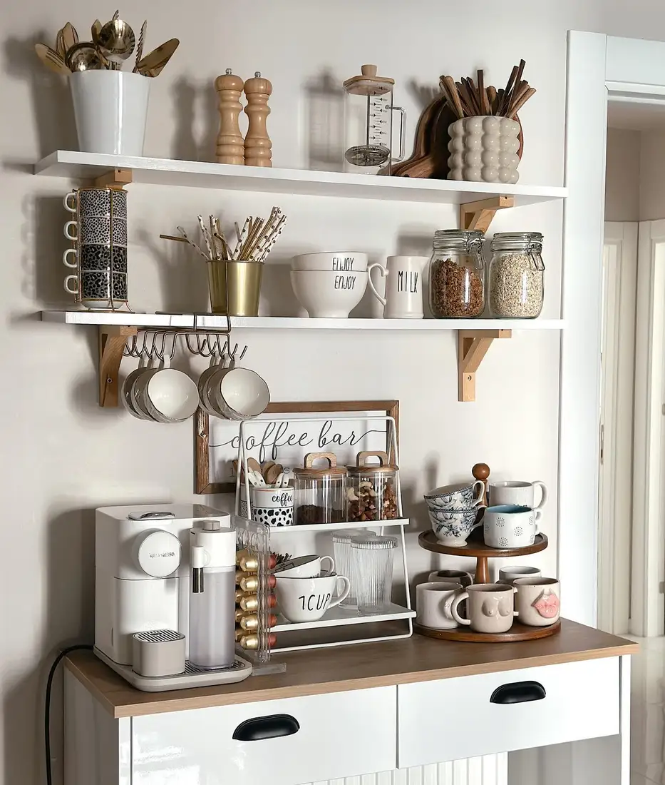 Coffee station with two white wall shelves, hanging mugs, coffee machine, storage jars, and tiered mug stand