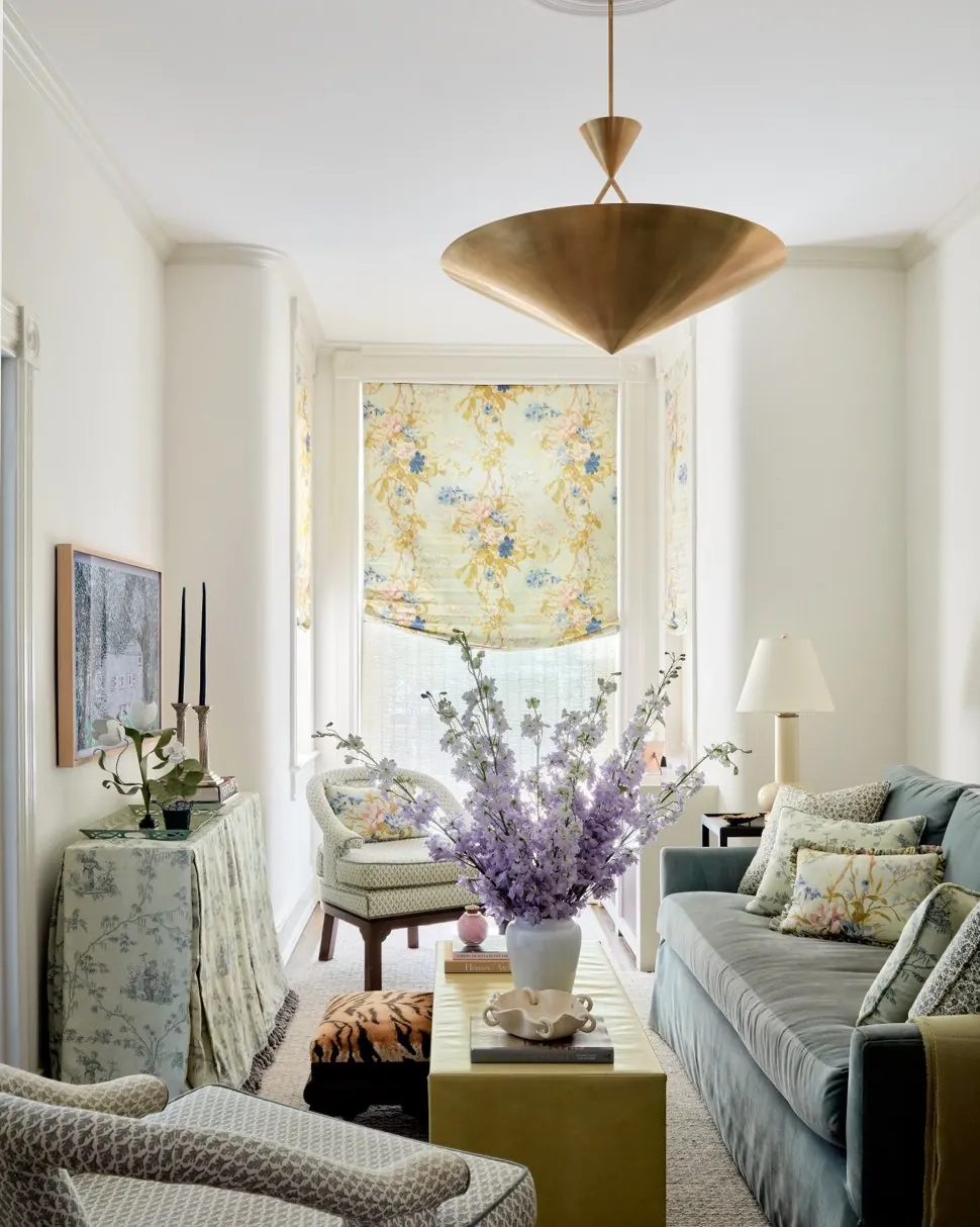 Cozy narrow living room with a sofa, woven chair, pink accent chair, and two small round tables