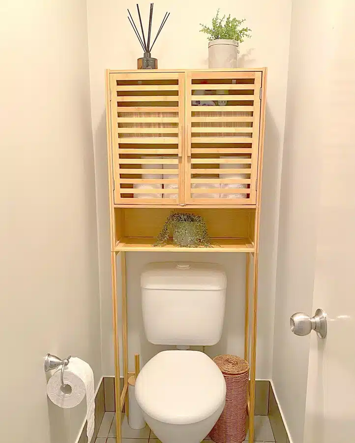 02 Tall wooden over-toilet cabinet with slatted doors, open shelf, plant, and bathroom storage