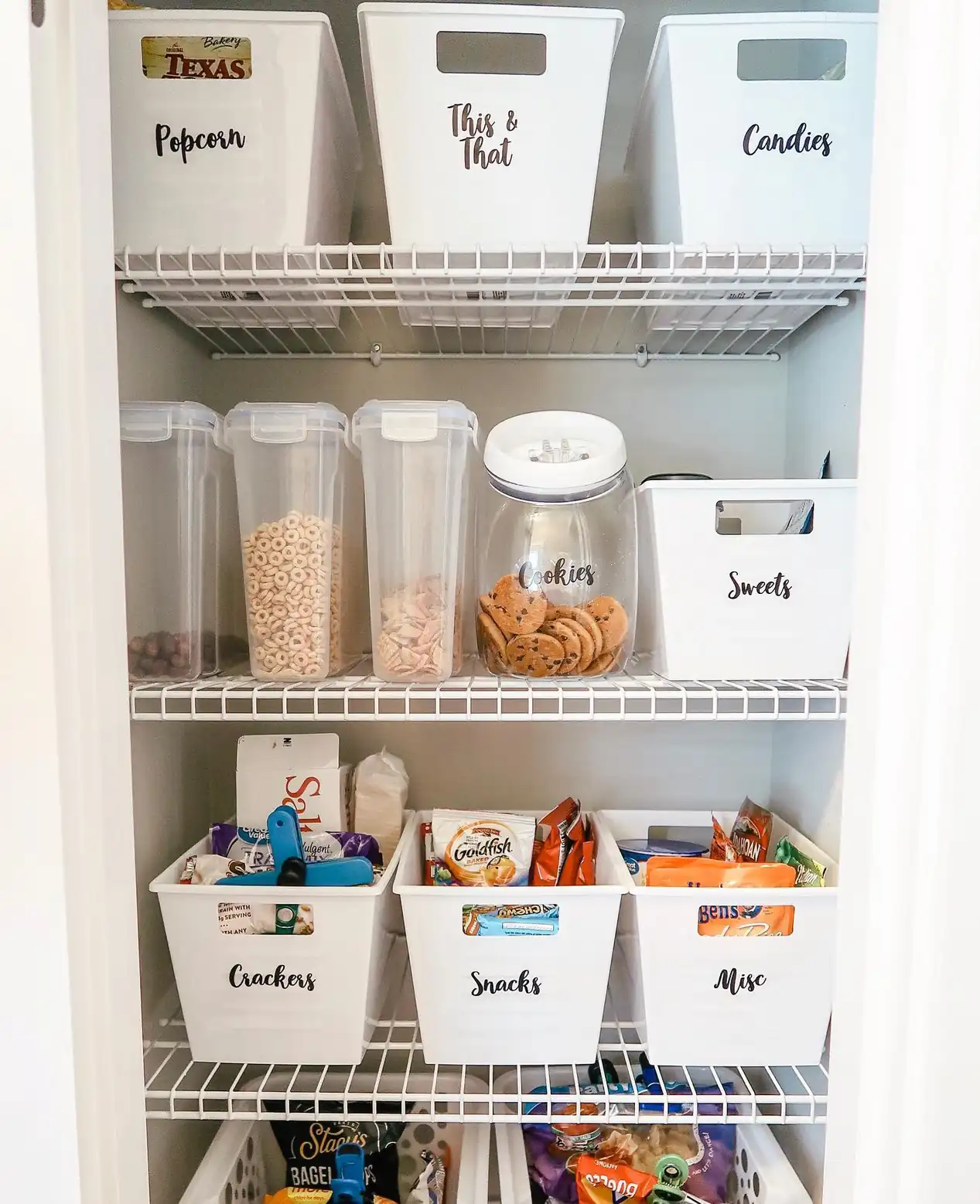 Labeled white pantry bins organizing snacks, crackers, sweets, and dry goods on deep pantry shelves